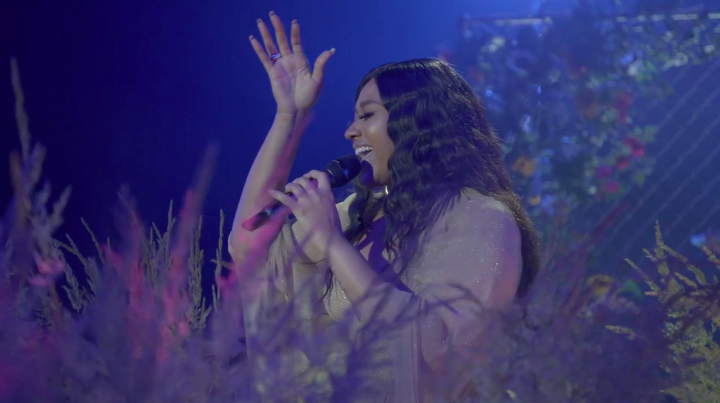 Singer Jazmine Sullivan singing on stage surrounded by flowers