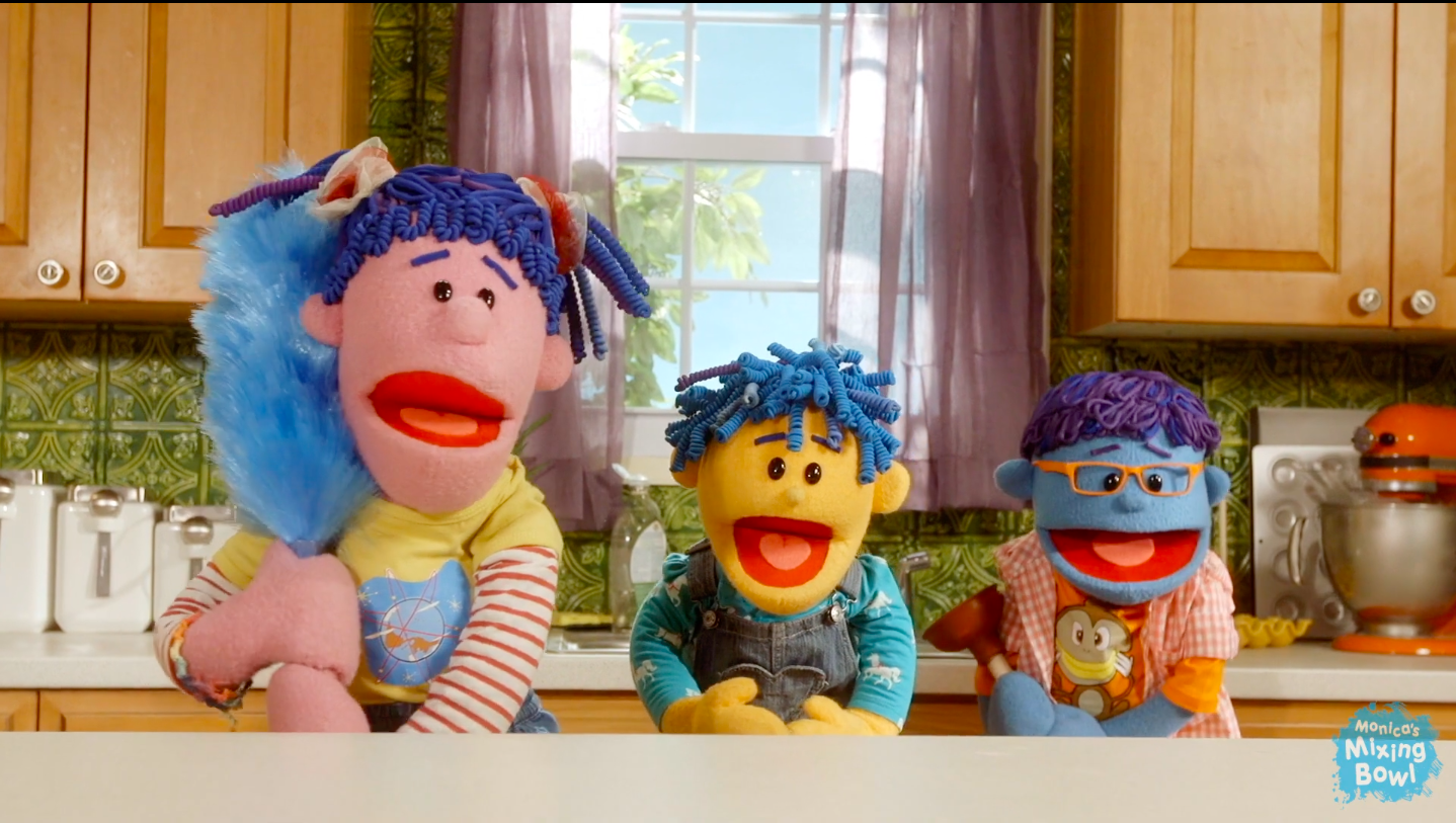 Three puppets, a girl, boy, and infant singing in the kitchen