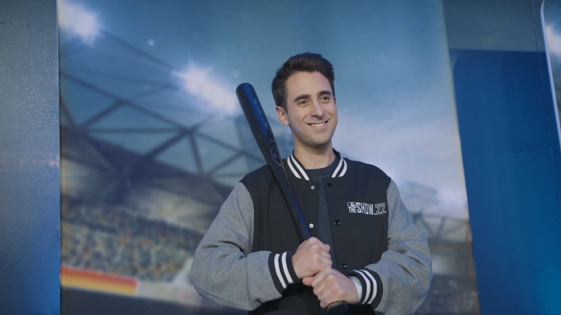 Host Jeff Eisenband holds baseball as he poses for a photo in front of a Dodger's Stadium backdrop