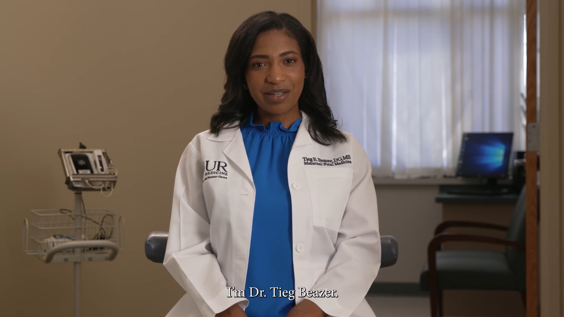 Dr in a white coast sitting in her office facing the camera to address it.