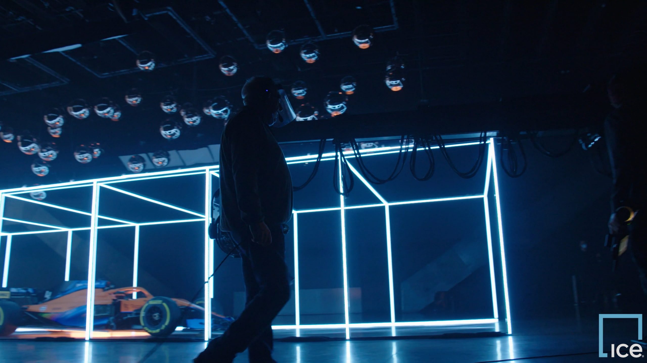 Camera assistant walking on set illuminated by bright blue lights with a race car in the background